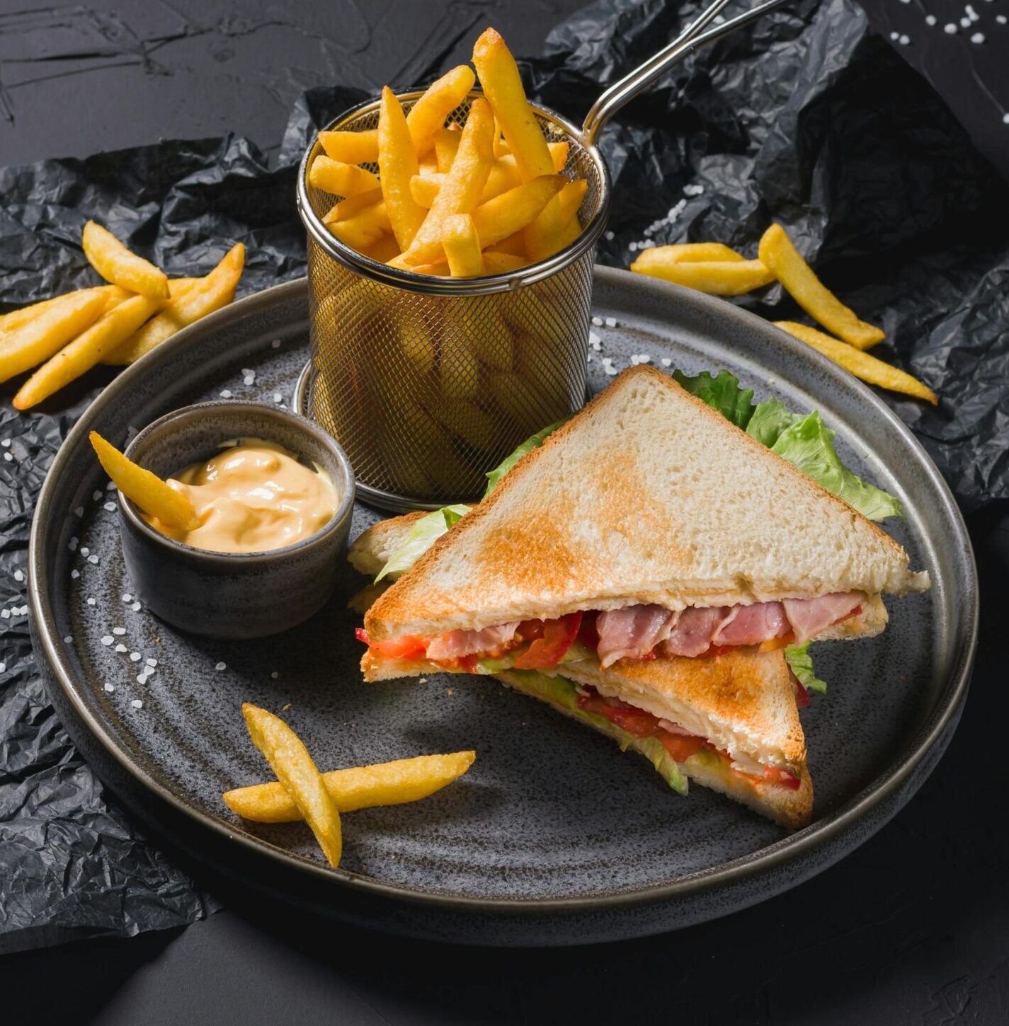 Close-up of a sandwich with fries on a rustic black surface. Perfect for foodies.