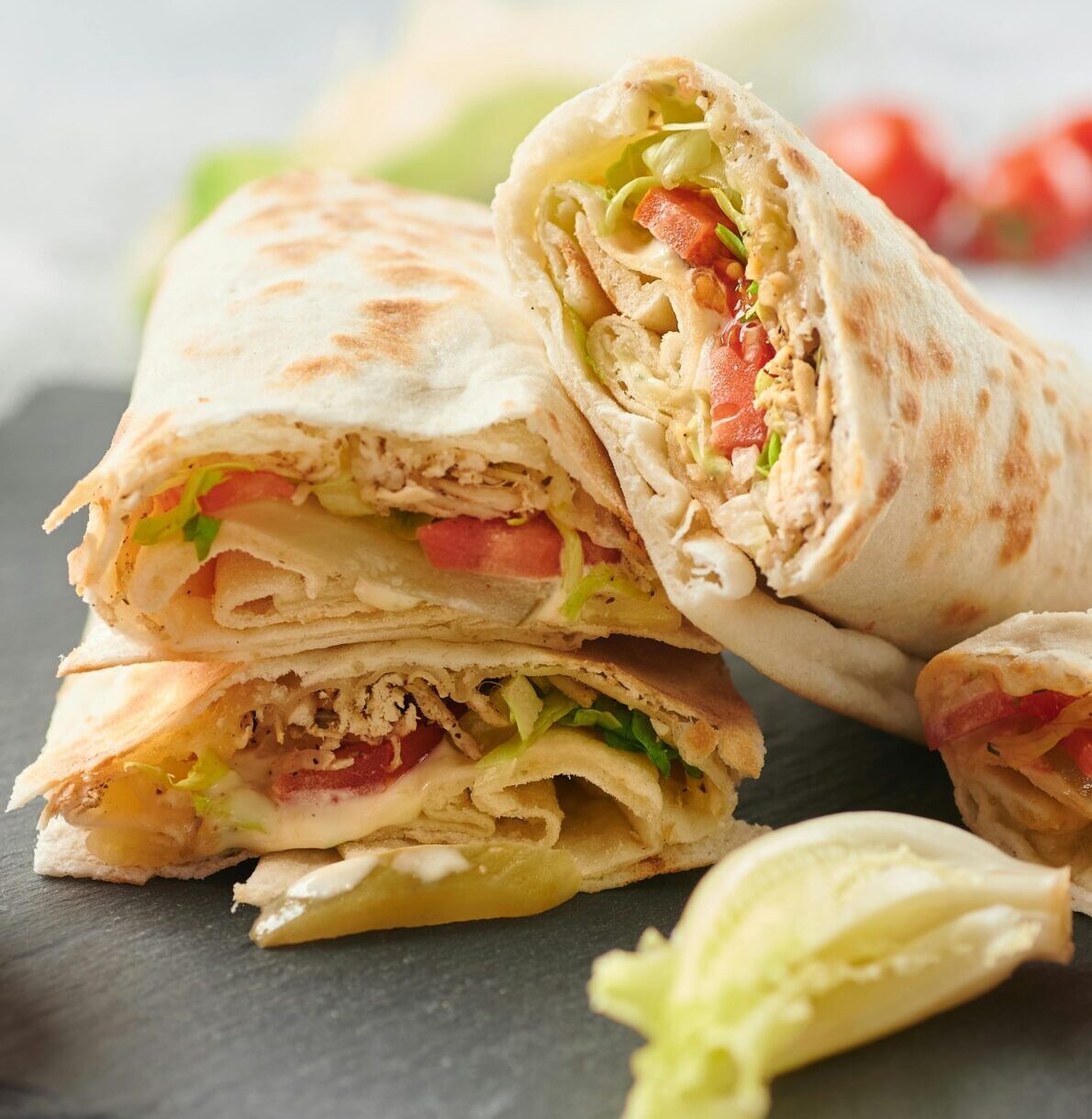 A tempting display of shawarma wraps with fresh lettuce, tomato, and sauce on a slate board.